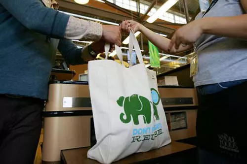Grocery store employee handing customer a bag of groceries in a reusable bag