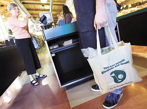 Grocery store check out bagger holding a custom printed reusable bag for customer