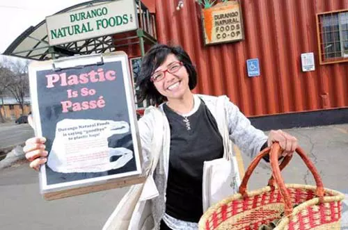 Woman smiling outside grocery store with anti-plastic bag sign