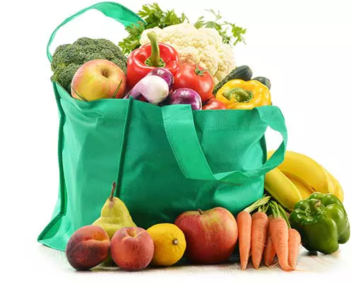 Green reusable shopping bag full of fruits and vegetables.