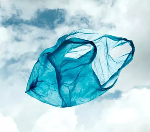 looking up at a single use plastic bag piece of litter floating through the air in front of clouds