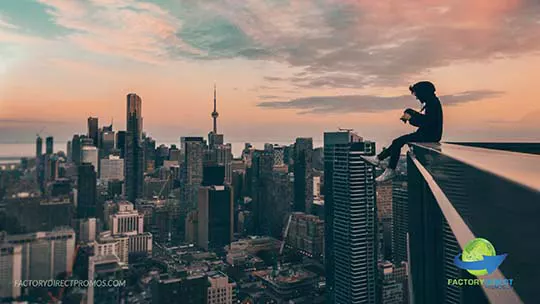 Photographer sitting on edge of high-rise building overlooking city skyline at sunset