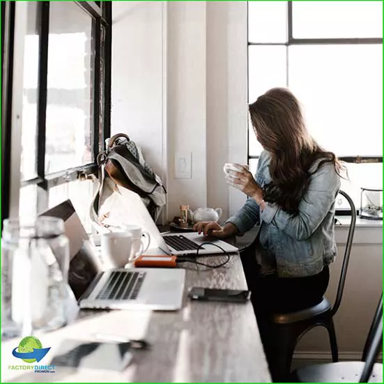 Woman sitting at a coffee bar working on a laptop near day lit windows