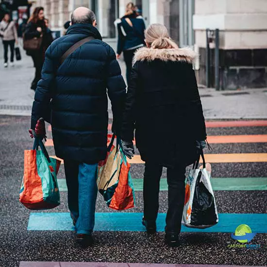 Two people carrying reusable shopping bags through a crosswalk