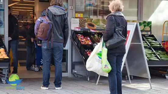 Woman with reusable bag standing outside grocery store practicing social distancing