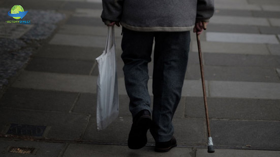 Elderly person with a cane walking on a sidewalk carrying a reusable bag