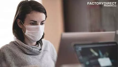 Female worker sitting at a computer wearing a mask to protect from COVID-19