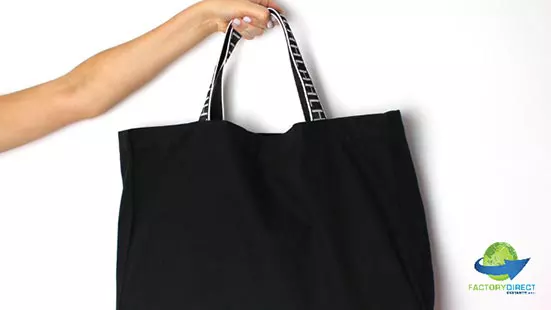 An outstretched arm holding a black reusable shopping bag