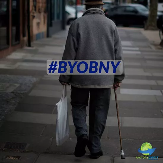 Older man with a cane walking on a New York City sidewalk carrying a bag