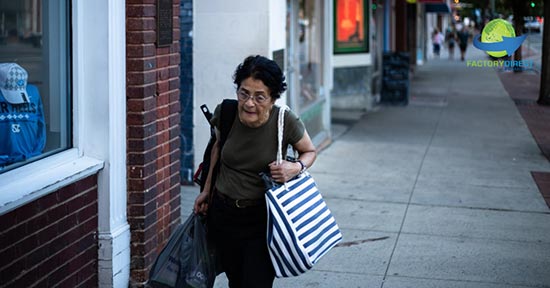 Elderly woman walking down the sidewalk carrying multiple types of bags